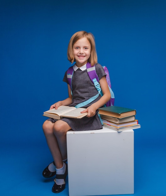 Uma estudante está sentada em um cubo branco e lendo um livro isolado em um fundo azul de volta à escola