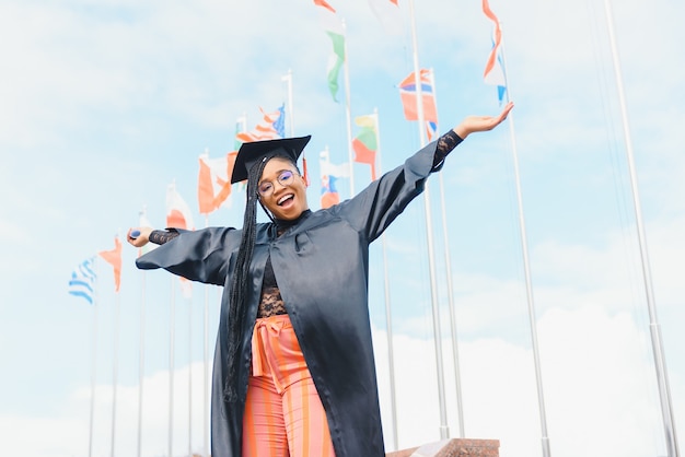 Uma estudante universitária africana com um boné e um vestido de formatura em frente ao prédio da escola