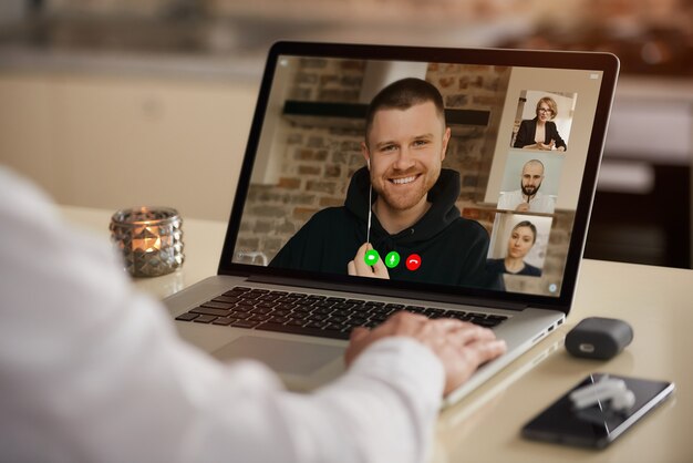 Foto uma exibição da tela do laptop do aplicativo de telecomunicações durante uma reunião on-line sobre o ombro de um homem.