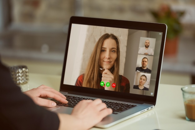 Uma exibição de tela de laptop sobre o ombro de uma mulher. uma menina está ouvindo uma declaração de sua colega em um briefing online