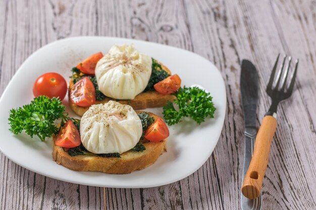 Uma faca e um garfo e duas fatias de pão frito com ovos pochê em uma mesa de madeira. Lanche vegetariano com ovos pochê.