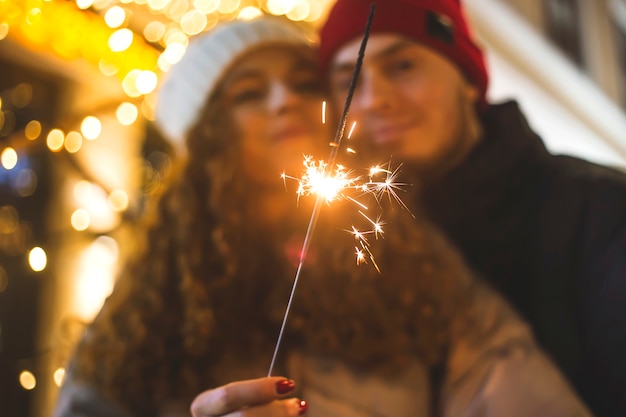 Uma faísca queima nas mãos de uma garota abraçada pelo namorado em um clima de Natal.