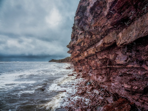 Foto uma falésia acima do mar com uma linha costeira estreita. ondas com espuma branca rolam no costão rochoso. costa de tersky, cape ship para a península de kola.