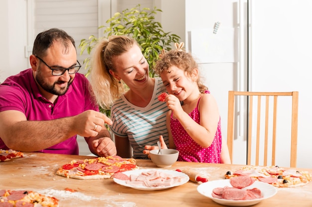 Foto uma família alegre a comer pizza em casa.