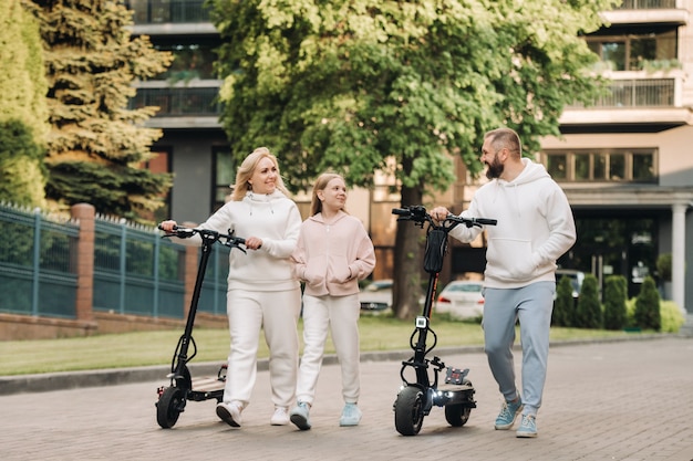 Uma família com roupas brancas anda de scooters elétricos pela cidade. atividades ao ar livre.