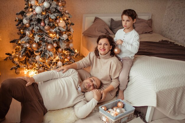 Uma família com uma criança em casa no quarto ao lado da cama perto da árvore de Natal.