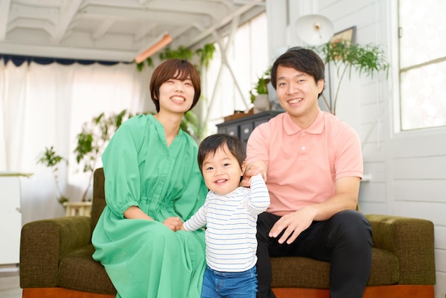 Uma família de três pessoas sorrindo e relaxando dentro de casa