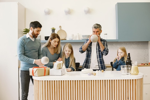 Uma família e duas filhas fazem uma festa. pessoas soprando balões. os presentes estão sobre a mesa.