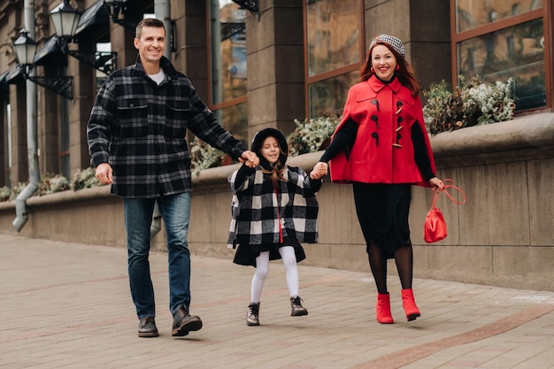 Uma família elegante de três passeios na cidade no outono de mãos dadas