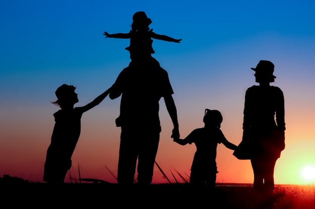 Uma família feliz à beira-mar ao pôr do sol em uma silhueta de viagens na natureza