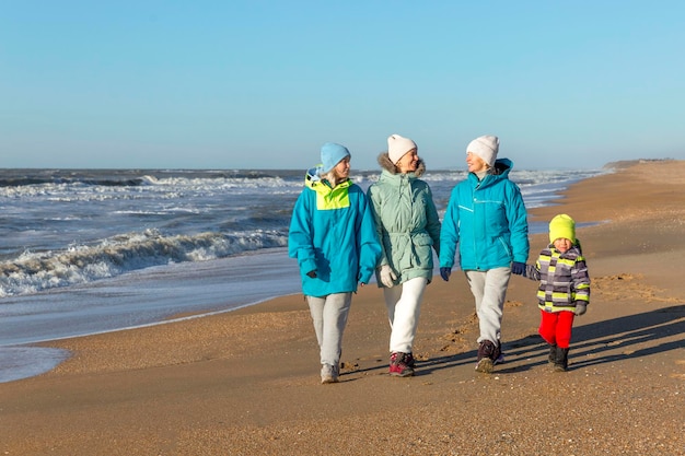 Uma família feliz caminha ao longo da praia de areia no inverno rindo mãe avó e filhos amor e ternura