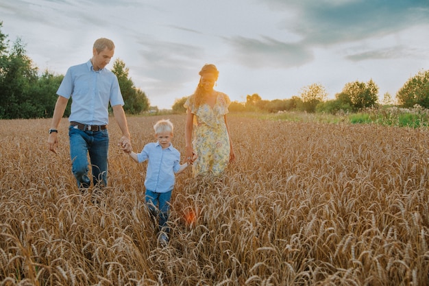 uma família feliz caminha por um campo de trigo se divertindo e rindo ao pôr do sol