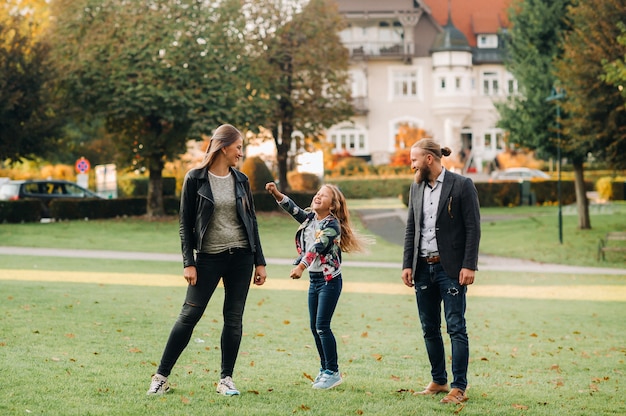 Uma família feliz de três pessoas corre pela grama na cidade velha da Áustria. Uma família caminha por uma pequena cidade na Áustria. Europa. Velden am werten Zee.
