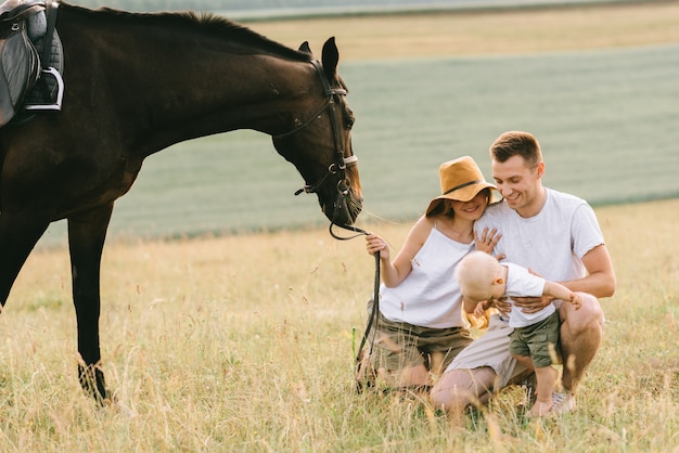 Uma família jovem se diverte no campo. pais e filho com um cavalo