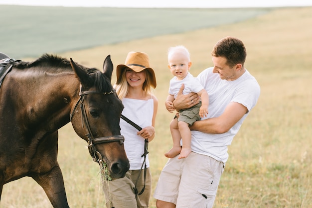 Uma família jovem se diverte no campo. pais e filho com um cavalo