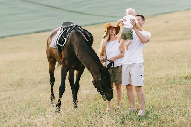 Uma família jovem se diverte no campo. Pais e filho com um cavalo