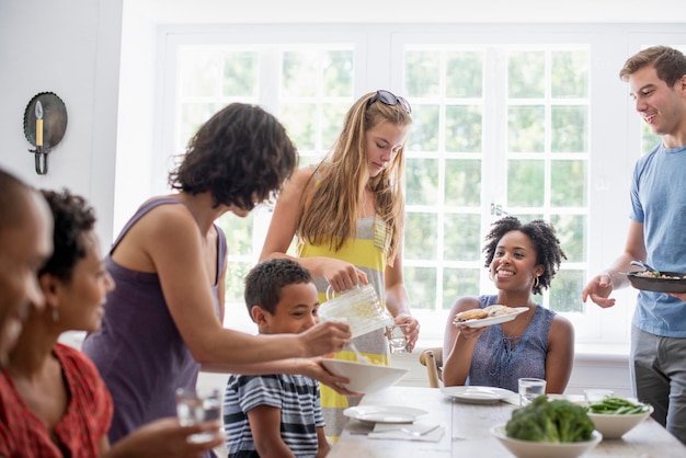 Uma família reunindo homens, mulheres e crianças ao redor de uma mesa de jantar compartilhando uma refeição