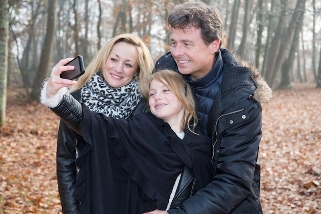 Uma família tira uma foto com um smartphone em um parque de outono