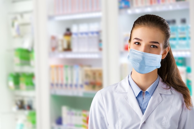 Uma farmacêutica com uma máscara médica posa no fundo de uma janela de farmácia