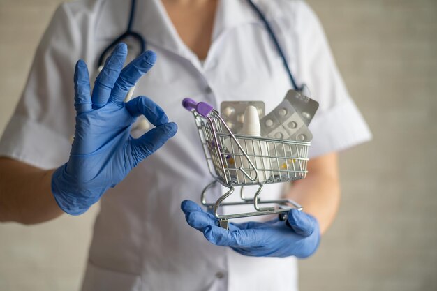 Uma farmacêutica sem rosto segura um mini carrinho de compras com medicamentos e gesticula com o ok Tomar vitaminas é a chave para uma boa saúde Recomendações do médico