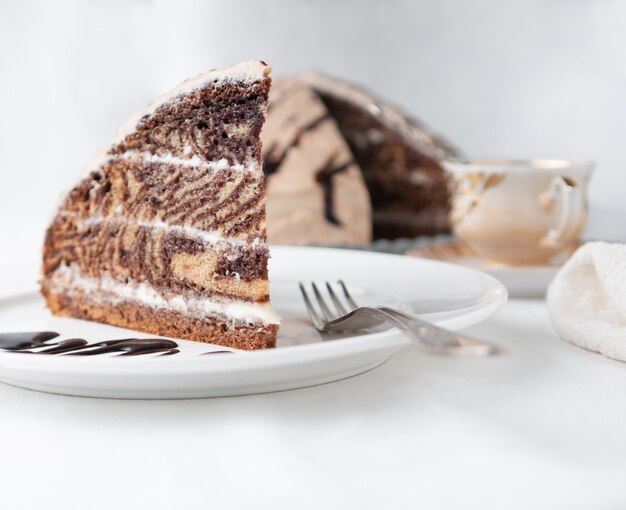 Foto uma fatia de bolo de mármore com creme guarnecido com glacê e chocolate em um prato branco com um garfo close