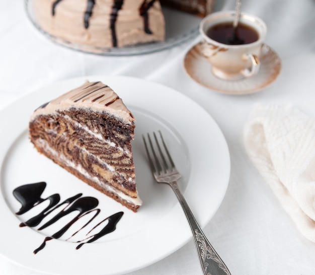 Uma fatia de bolo de mármore com creme Guarnecido com glacê e chocolate Em um prato branco com um garfo Close