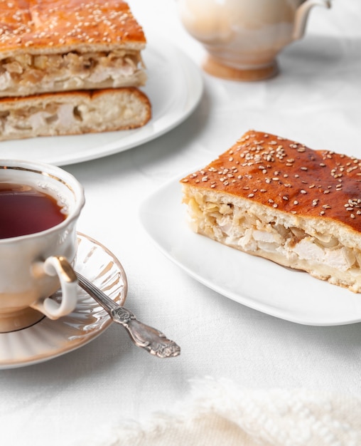 Uma fatia de frango caseiro com torta de gergelim. num prato branco. perto de uma cafeteira e uma xícara de café. fundo branco.