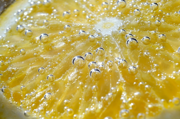 uma fatia de laranja coberta com bolhas encontra-se em um copo de água com gás. Fechar-se.