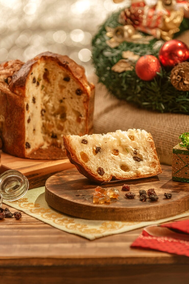 Foto uma fatia de panetone e cubos de frutas cristalizadas em uma tábua de madeira com enfeites de natal