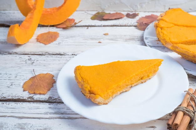 Uma fatia de torta de abóbora americana e abóbora em uma mesa de madeira branca Comida tradicional de outono