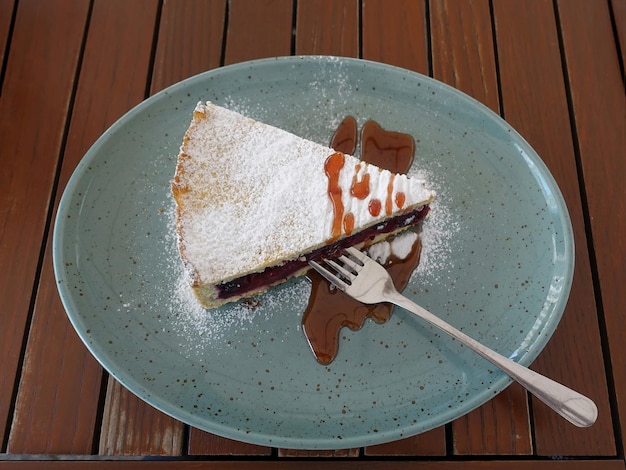 Uma fatia de torta de cereja coberta de açúcar e calda em um prato com um garfo na mesa