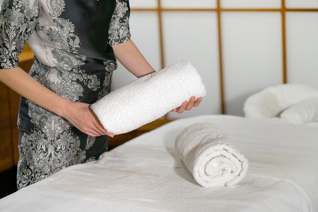 Uma faxineira dobra uma toalha em uma cama de massagem.