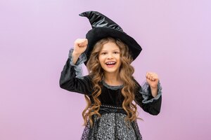 Uma feiticeira surpresa e alegre em uma fantasia preta em um fundo isolado uma garotinha em uma fantasia de bruxa com cabelo encaracolado