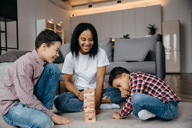 Uma feliz família negra, mãe e dois filhos brincando com uma rodada de jenga