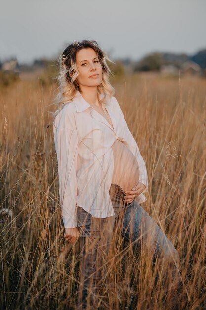 Uma feliz futura jovem mãe é uma mulher de roupas brancas com uma grande barriga de grávida paisagem natural o conceito de gravidez