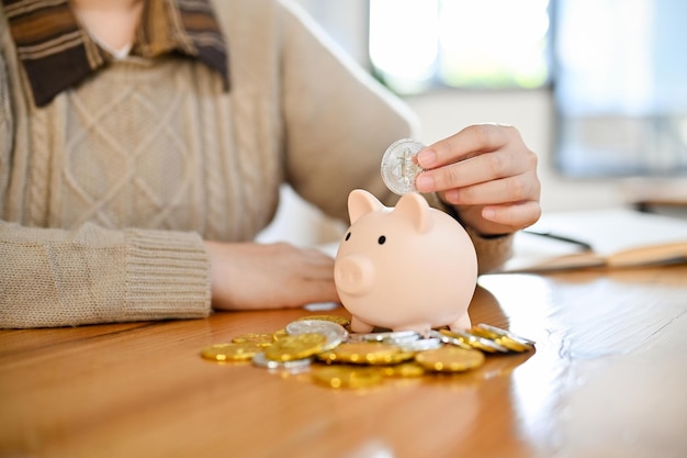 Uma fêmea insere moedas em um cofrinho economizando dinheiro e conceito de investimento cortado
