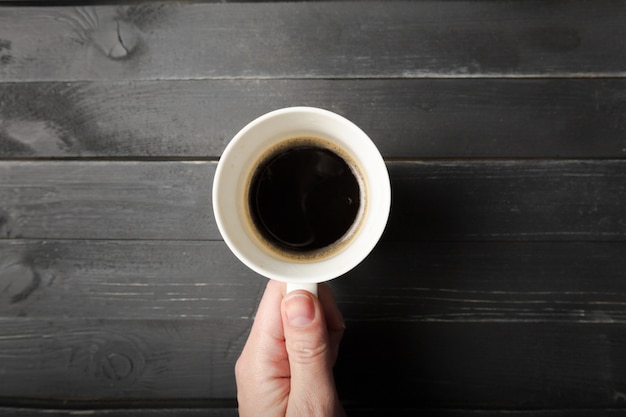 Uma fêmea mãos segurar uma xícara de café na mesa de madeira