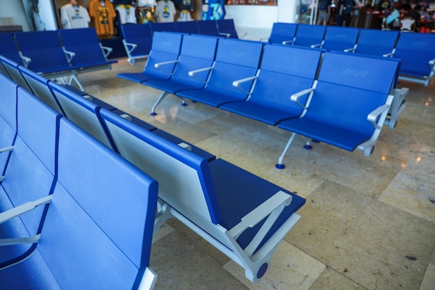Uma fileira de cadeiras azuis em um terminal com uma placa que diz 'aeroporto'