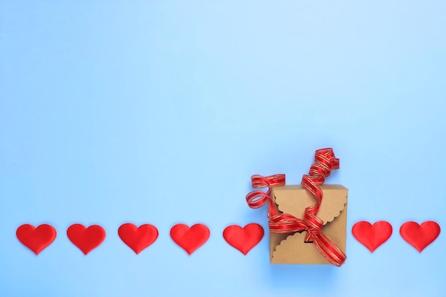 Uma fileira de corações em um fundo azul com uma caixa de presente amarrada com uma fita vermelha Copie o espaço