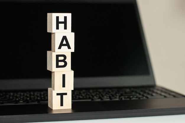 Uma fileira de cubos de madeira com a palavra HÁBITO escrita em fonte preta está localizada em um teclado preto. Texto HABIT