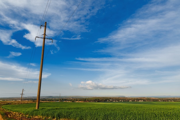 Uma fileira de postes de uma linha de energia em um campo perto de uma estrada de terra sob um céu claro, linha de transmissão de eletricidade, fonte de alimentação