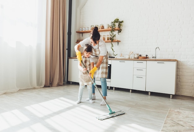 Uma filhinha e sua mãe limpam a casa uma criança lava o chão da cozinha uma linda ajudante limpa o chão com um esfregão uma família feliz limpa o quarto