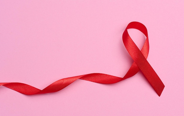 Uma fita de seda vermelha em forma de laço sobre fundo rosa, símbolo da luta contra a AIDS e sinal de solidariedade e apoio