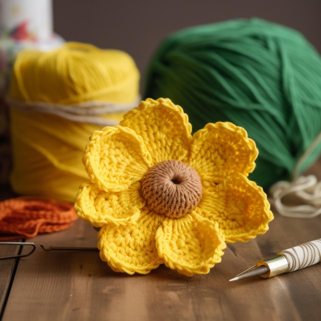 Uma flor amarela feita de lã está sobre uma mesa ao lado de um novelo de lã.