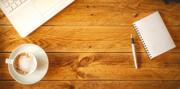 Uma folha de papel em branco com uma caneta sobre uma mesa de madeira com uma xícara de café.