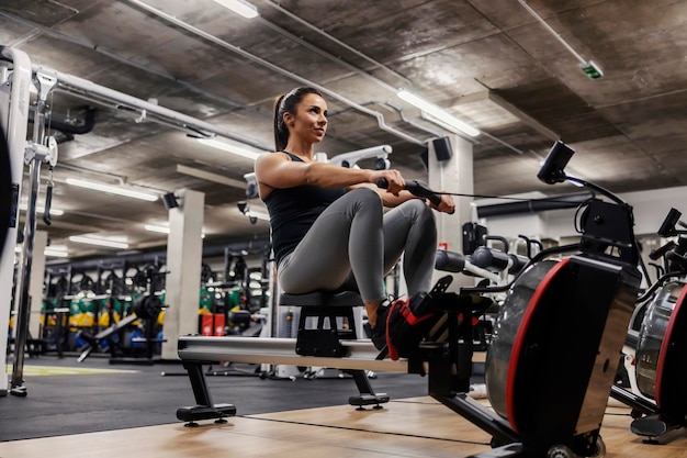 Uma forte desportista está fazendo exercícios para as pernas em uma máquina de remo