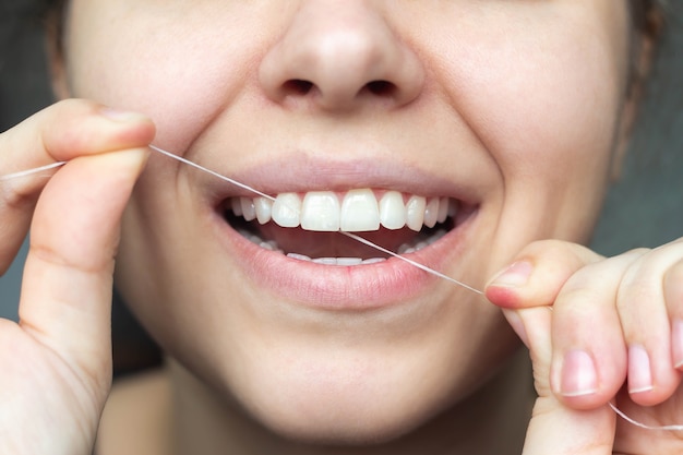 Uma foto cortada de uma bela jovem passando fio dental nos dentes. Fechar-se. Conceito odontológico