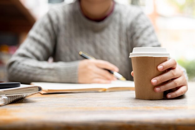 Uma foto cortada de uma mulher a beber café e a trabalhar remotamente num café.