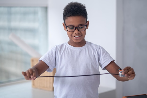 Uma foto da cintura para cima de um menino com um cabo usb nas mãos