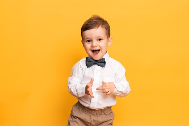 Uma foto de estúdio de um menino bonitinho fazendo careta fica em um fundo amarelo. Garoto engraçado